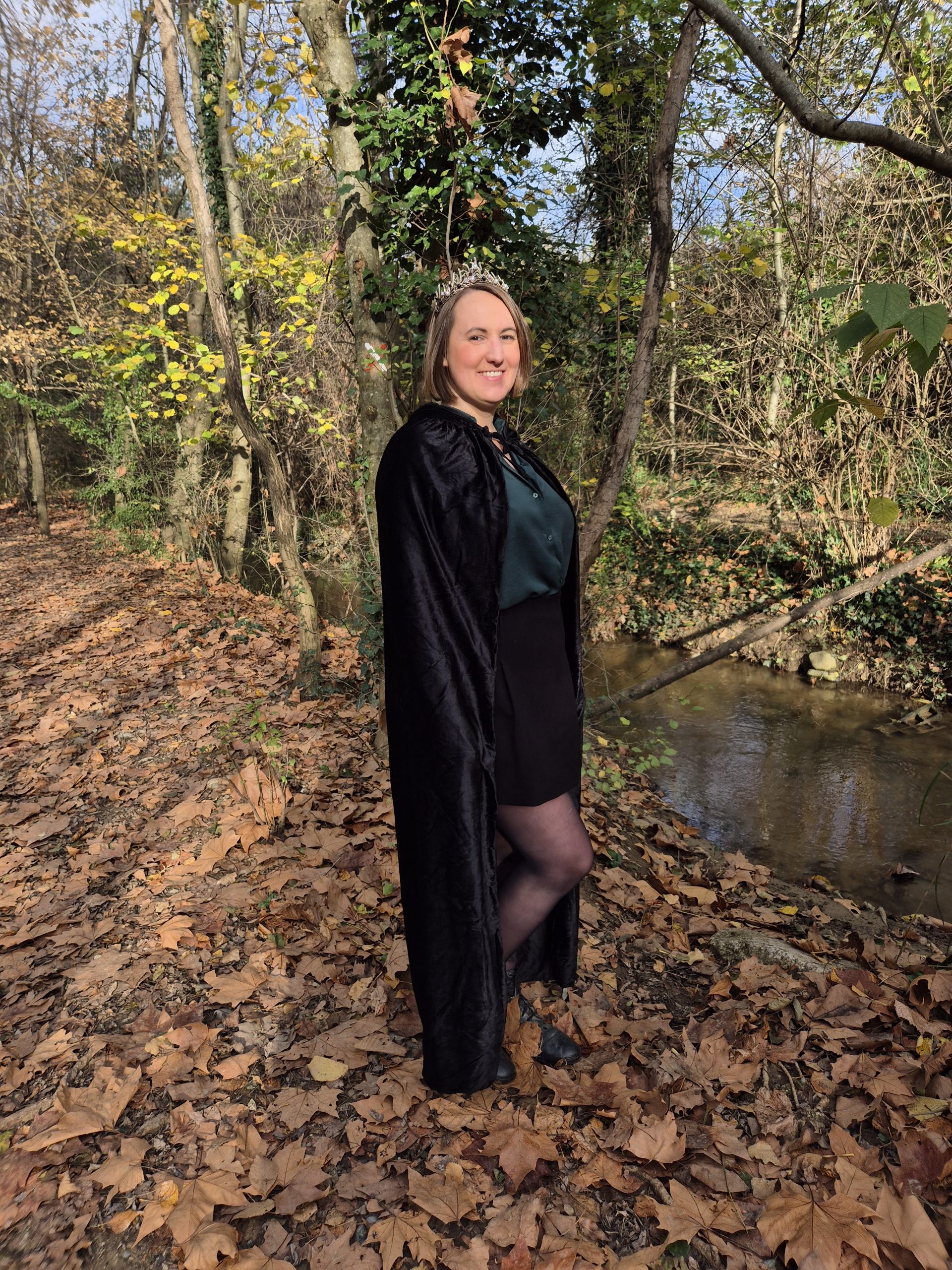 Gwen en cape de sorcière et couronne dans la nature, accompagnante en confiance en soi, exploration de l’invisible et transformation spirituelle.