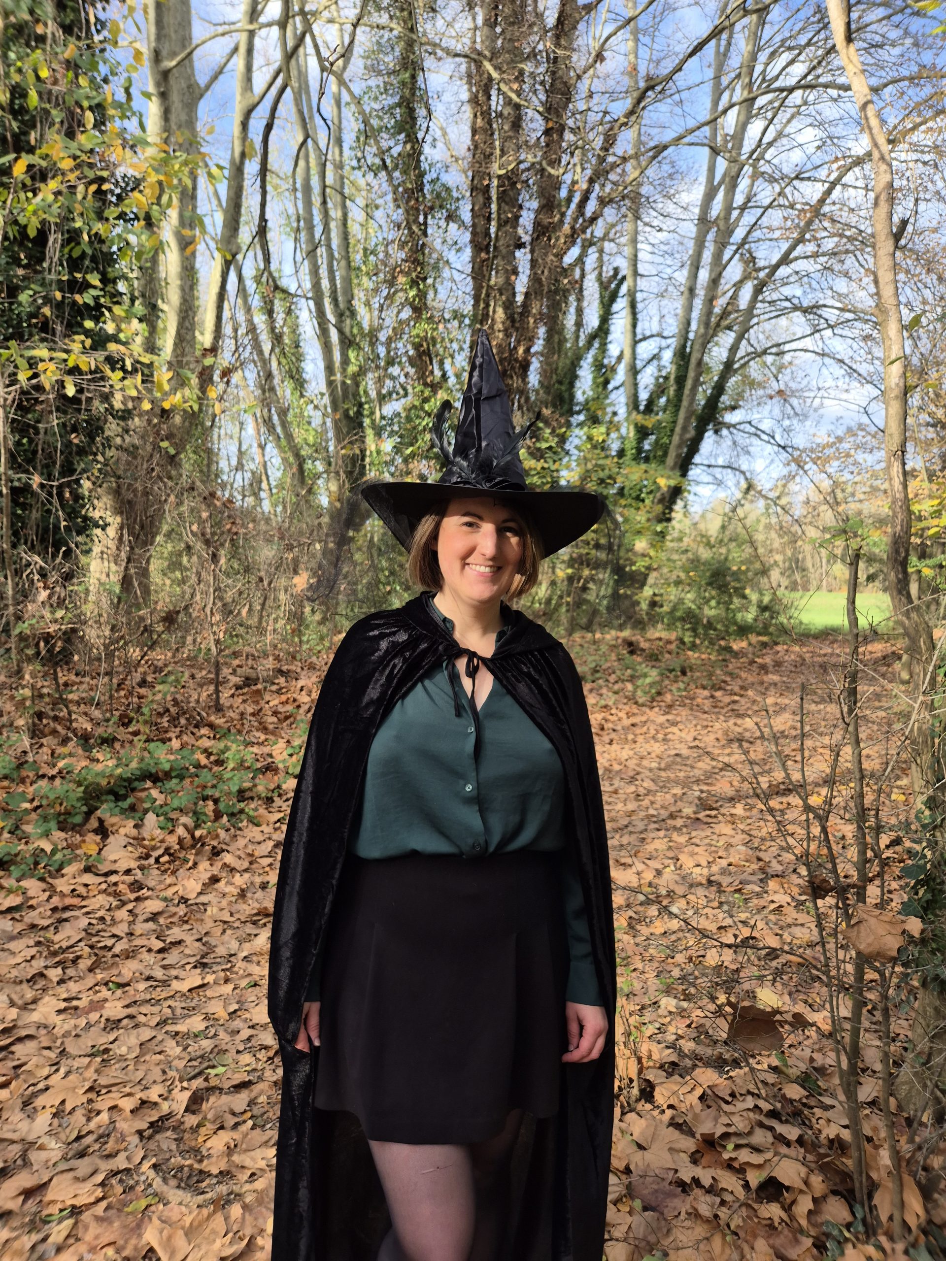 Gwen en cape et chapeau de sorcière, debout dans la nature, accompagnante du programme RÉVÉLATIONS pour explorer l’invisible en sécurité.