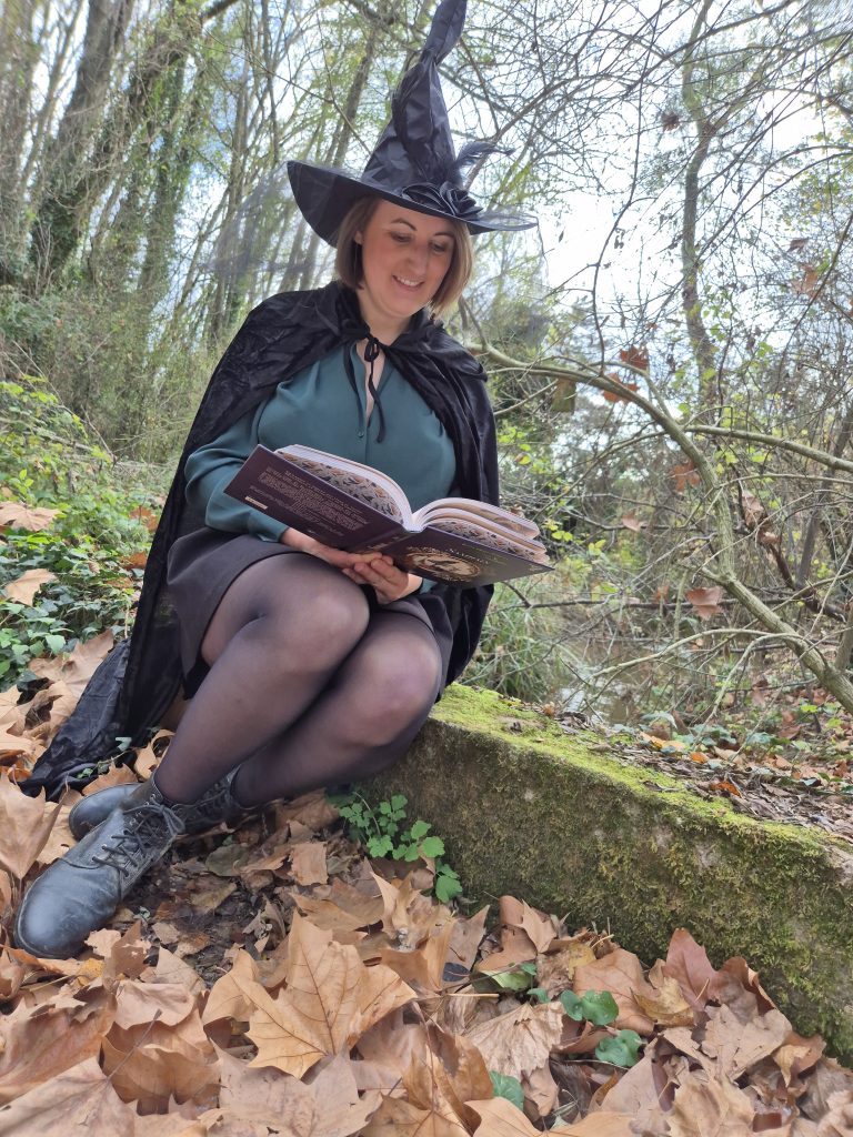 Une photo de moi lisant un livre sur le sabbat de Samhain, avec chapeau et cape de sorcière, dans la nature