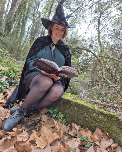 Une photo de moi lisant un livre sur le sabbat de Samhain, avec chapeau et cape de sorcière, dans la nature